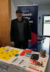 A person standing in front of a table with papers and a sign

Description automatically generated