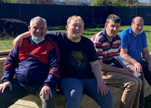 A group of men sitting on a wooden bench

Description automatically generated