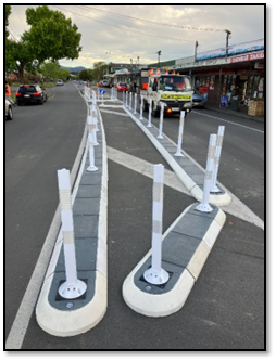 A row of white poles on a street

Description automatically generated