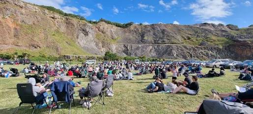 A large group of Carols in the Quarry attendees sitting on a grass area.
