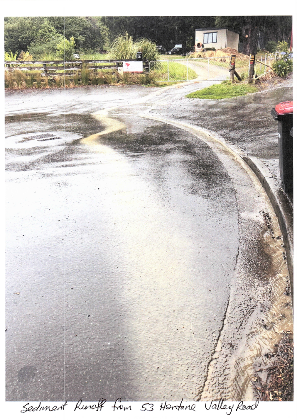 A wet road with a sign and a fence

Description automatically generated with medium confidence
