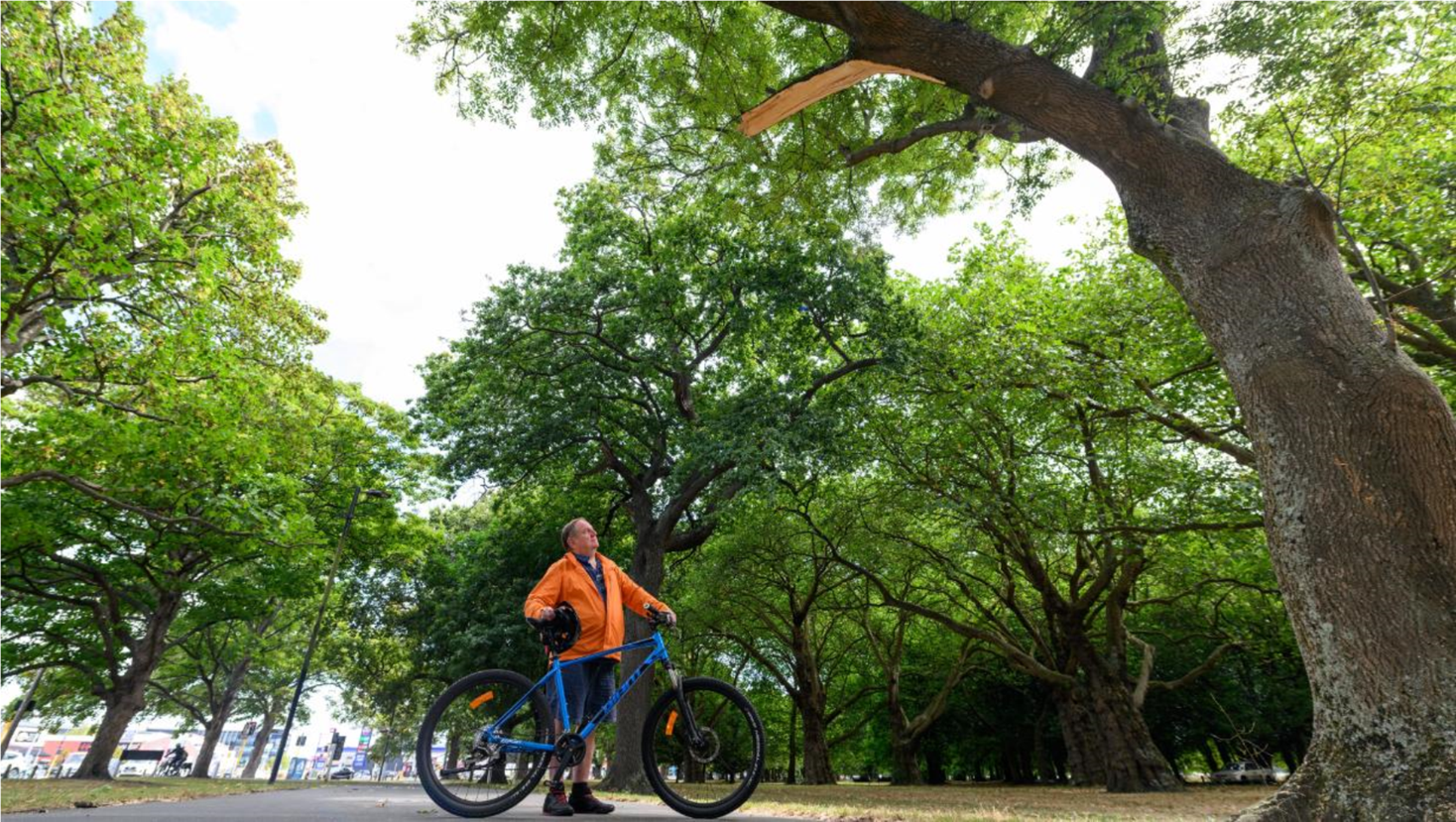 A person in an orange jacket holding a blue bike

Description automatically generated