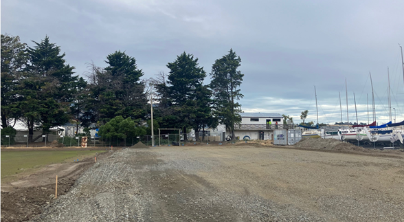 A dirt road with trees and buildings in the background

Description automatically generated