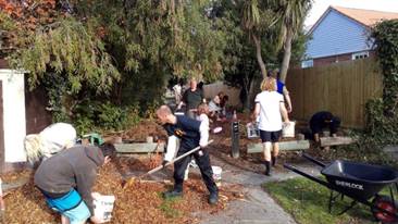 A group of people moving mulch, raking and clearing ground at an entrance pathway to Harrington Park.
