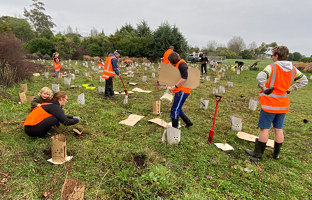 A group of people in orange vests working in a field

Description automatically generated
