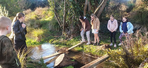 A group of people standing on a bridge over a stream

Description automatically generated