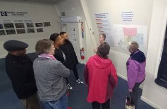 A photo of 7 people standing together and talking in a room.