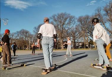 A person speaking to a group of people (in a circle on skateboards) outside on a netball court.