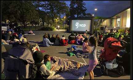 A group of people sitting in a park watching a movie

Description automatically generated