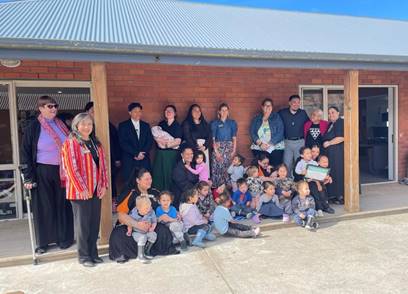 A group of adults and children, including board members, gathered outside a Kohanga Reo, posing for a photo.

