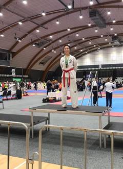 Wen-Qi  standing on a platform wearing medals in a sports hall.
