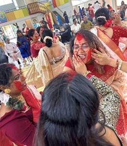 A large group of people in a hall wearing traditional attire and a number of women with red paint on their face.

