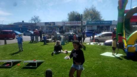 Families and children enjoying activities (bouncy castle and playing games) on a grassed area.
