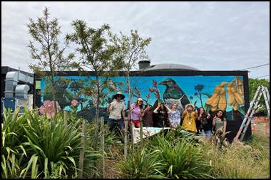 A group of people posing for a picture in front of a mural

Description automatically generated
