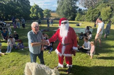A group of people sitting in an open grassed area seated and standing and person dressed as Santa Claus shaking hands with a resident.

