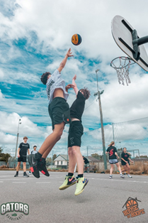 A group of people playing basketball with two children jumping, one shooting a basketball and one defending