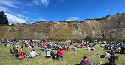 A large group of people seated on the grass in an open space at Halswell Quarry.