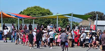 A crowd of people outside surrounding Santa Clause and a car