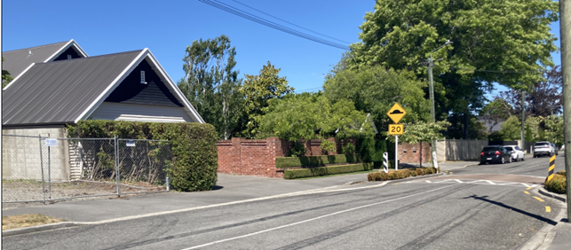 A road with a brick wall and a sign

Description automatically generated