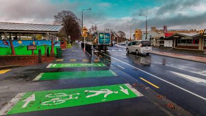 A wide view of Riccarton Road showing traffic and a shared cycle and pedestrian path outside the exit from Woolworths onto Riccarton Road.

