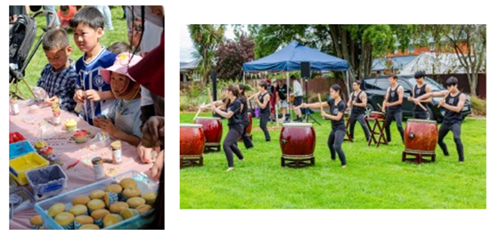 A group of children standing at a table decorating cupcakes and a group of people playing drums on a grassed area.